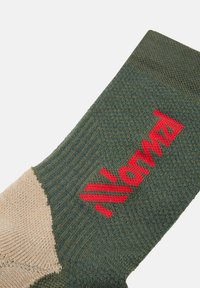Calcetín verde con detalles beige, textura de punto y logotipo rojo "Noruega". Bloques de color distintivos y diseño acanalado que mejoran la funcionalidad.