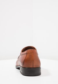 Brauner Lederschuh mit strukturiertem Finish, runder Spitze, flacher schwarzer Sohle und dezenten Stichdetails an der Oberseite.