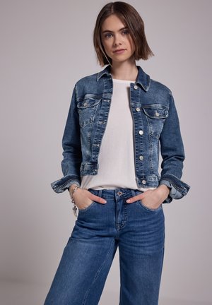 Jeansjack met een lichtblauwe wassing, voorzien van een kraag, knoopsluiting, twee borstzakken en opgerolde mouwen. Gecombineerd met hoog getailleerde blauwe jeans.