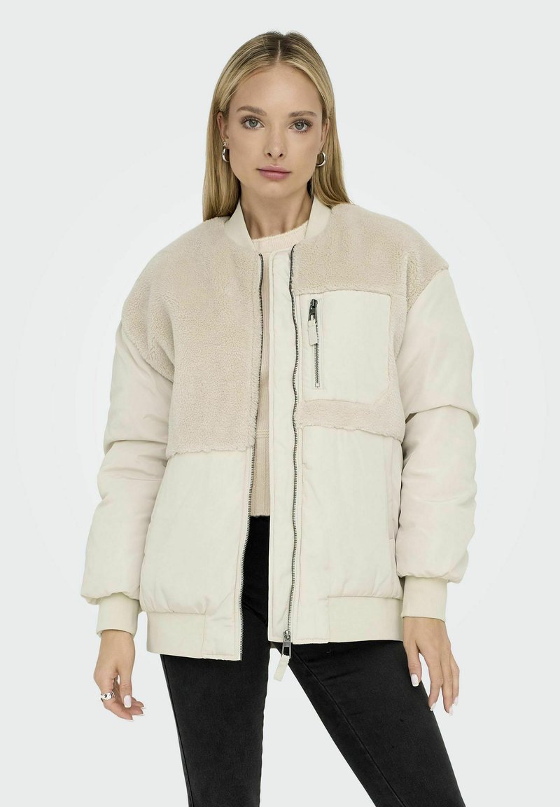 Giacca bomber beige chiaro con pannello superiore plush e testurizzato, chiusura frontale con zip, dettagli di tasche e polsini e orlo a coste.