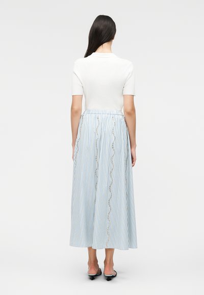 Γυναίκα με μακριά σκούρα μαλλιά που φοράει λευκό τοπ με κοντά μανίκια και μπλε-λευκή ριγέ φούστα μέχρι τον αστράγαλο με κυματιστό κατακόρυφο κέντημα.