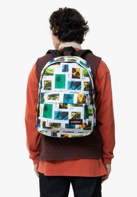 Ryggsäck med ett fotografiskt tryck i grönt, blått och gult på en vit bakgrund. Inkluderar en framsidig ficka och vadderade axelremmar.