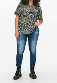 Maglietta a maniche corte con stampa leopardata in marrone e nero, abbinata a jeans skinny blu medio e stivali neri con lacci.