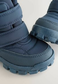 Dunkelblaue isolierte Stiefel mit Obermaterial aus strukturiertem Stoff, Klettverschlüssen und robusten Gummisohlen mit ausgeprägten Profilen für Halt.
