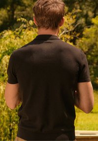 Musta lyhythihainen poolopaita, jossa on yhtenäinen kangas ja kaulus. Selkäpuolen muotoilu on istuva, korostaen siistiä siluettia.