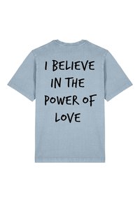 T-shirt en coton bleu clair avec des manches courtes et un col rond. Présente un texte noir audacieux dans le dos : "JE CROIS EN LE POUVOIR DE L'AMOUR."