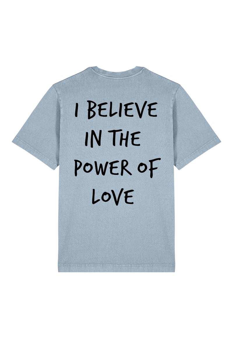 T-shirt en coton bleu clair avec des manches courtes et un col rond. Présente un texte noir audacieux dans le dos : "JE CROIS EN LE POUVOIR DE L'AMOUR."
