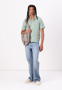 Lichtgroen shirt met korte mouwen, relaxte pasvorm, grijze schoudertas, blauwe flared jeans, beige schoenen met rubberen zool. Soepele textuur, casual stijl.