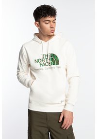 Sudadera color crema con un bolsillo frontal, que presenta un logo y texto en verde. Hecha de algodón, cuenta con capucha con cordón y puños acanalados.