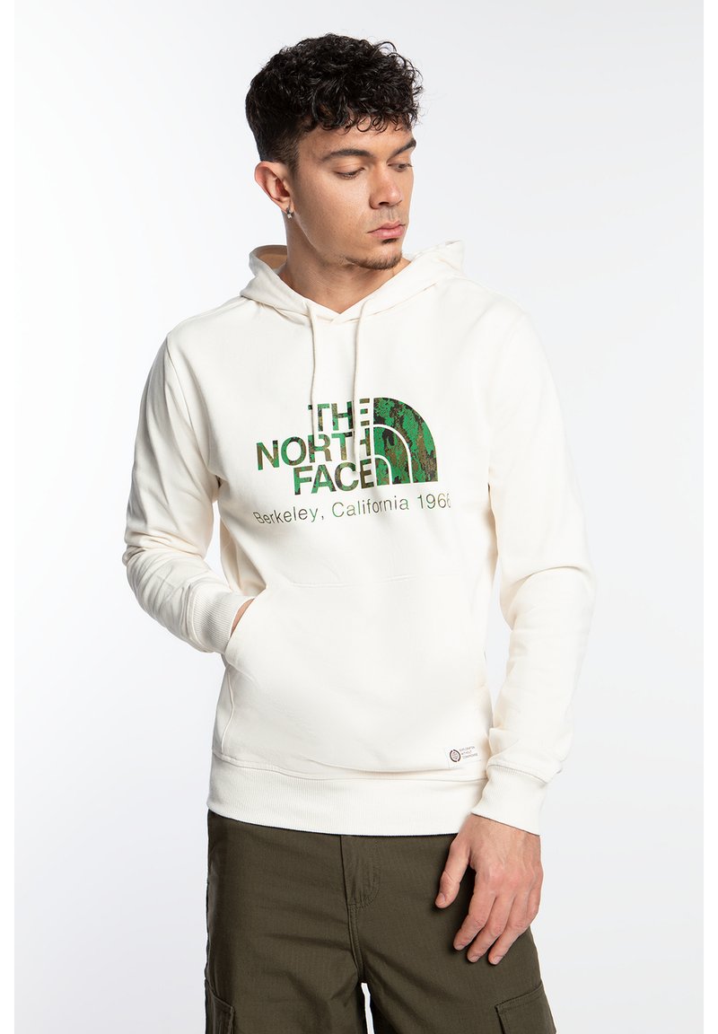 Sudadera color crema con un bolsillo frontal, que presenta un logo y texto en verde. Hecha de algodón, cuenta con capucha con cordón y puños acanalados.