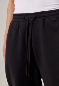 Zwarte sweatpants van zachte stof; voorzien van een elastische tailleband met een trekkoord, subtiele textuur en zijzakken.