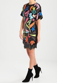 Svart kortärmad klänning med färgstarka, paljetterade stjärn- och bokmönster, med en rundad halsringning och en något utsvängd silhuett.