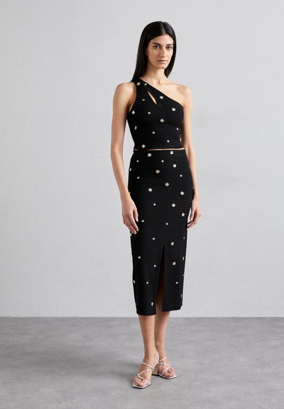 Ensemble noir deux pièces composé d'un crop top asymétrique et d'une jupe midi, ornée de petits embellissements floraux dorés et d'une fente à l'avant.