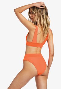 Oranžový rebrovaný bikiny set so zvýšeným pásom a bezrukávovým topom s hlbokým vykrojením na chrbte. Hladká textúra a minimálne kovové prvky.