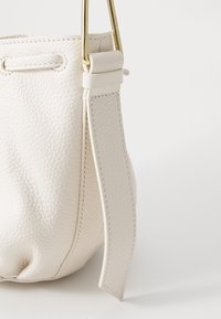 Borsa a secchiello bianca in pelle con superficie texturizzata, hardware dorato e ampia tracolla. Presenta una chiusura con coulisse e cuciture a contrasto.