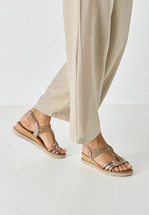 Bronzefarbene Sandalen aus Metallic-Material mit Keilabsatz aus Kork, mehreren Riemen und einer strukturierten Oberseite. Flache Sohle, offenes Zehendesign und verstellbarer Fersenriemen.