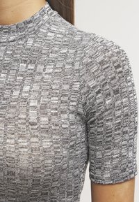 Harmaa neulepaita, jossa on puolikorkea kaulus. Paidassa on neliö- ja suorakaiteenmuotoinen tekstuurikuviointi, lyhyet hihat ja istuva leikkaus.