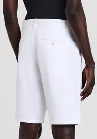 White tailored shorts featuring a smooth fabric, a straight cut, two back pockets with button closures, and a belt loop waistband.