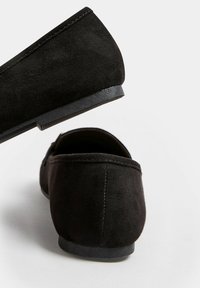 Ballerine nere in suede con profilo basso, punta rotonda e suola in gomma liscia. Presentano cuciture discrete lungo i bordi e una texture morbida.