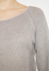 Hellgrauer Strickpullover mit weit ausgestelltem Bootsausschnitt, strukturiertem Material und subtilen Glitzereffekten sowie offenen Strickdetails an den Schultern.