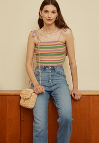 Top de crochê cropped em listras multicoloridas, com alças de ombro; combinado com jeans de cintura alta azuis e uma bolsa de palha bege com uma alça de corrente.