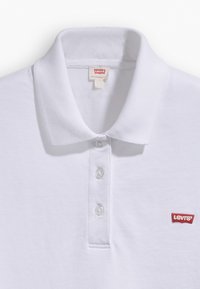 Polo blanc Levi's avec une patte de boutonnage à trois boutons et un écusson logo Levi's rouge sur la poitrine gauche.