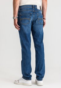 Niebieskie dżinsy o regularnym kroju, z pięcioma kieszeniami i kontrastującymi szwami. Noszone z białymi trampkami, podwinięte przy kostce.