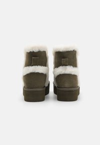 Bottes de cheville en daim vert avec un bord en fourrure blanche. Semelle en caoutchouc et talon plat. Design simple avec un petit détail de languette à l'arrière.