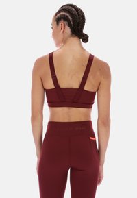 Bordeaux sportovní podprsenka se širokými ramínky a texturovaným vzorem, doplněná o odpovídající bordeaux legíny s vysokým pasem a oranžovým akcentem.