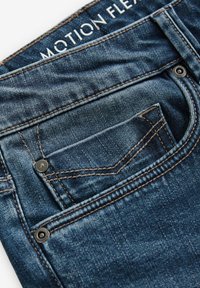 Džínsy z denimu s tmavým umývaním, zdobené oranžovým šitím a kovovými detailmi na zadnej vrecku. Štítky označujú "MOTION FLEX."