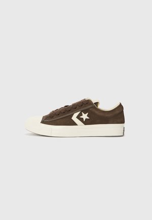 Brown suede sneakers with a white rubber toe cap, flat laces, and a triangular logo featuring a star on the side.