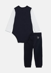 Body en coton marine pour bébé avec des manches longues blanches et un pantalon assorti. Présente un petit logo sur le pantalon. Design doux et décontracté.