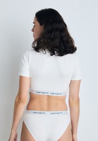 Haut ajusté à manches courtes blanc et culotte assortie avec une bande élastique à logo. Texture lisse, design minimaliste et sans motifs.