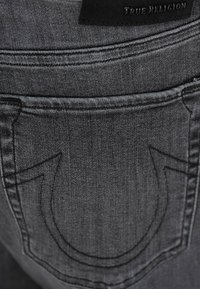 Czarne dżinsy typu denim z tylną kieszenią wyróżniającym się krzywym przeszyciem oraz skórzaną metką marki w okolicy pasa.