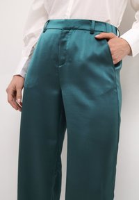 Teal satinbyxor med en slät yta, framfickor och en skräddarsydd passform, stiliserade med en vit skjorta, som har en figursydd midjeband.