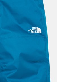 Tecido azul com costuras visíveis, apresentando um logo branco "The North Face" do lado direito.