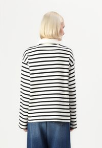 Black and white striped long-sleeve top with a collar, featuring a relaxed fit and a plain back, paired with blue denim trousers.