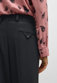 Black trousers with a textured finish, featuring a small triangle pocket and button detail. Complemented by a pink blouse with butterfly prints.