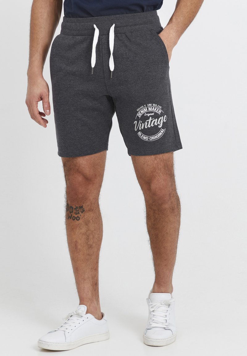 Shorts en coton gris avec une taille élastique et un cordon blanc, arborant un logo et un texte imprimés sur la cuisse gauche.
