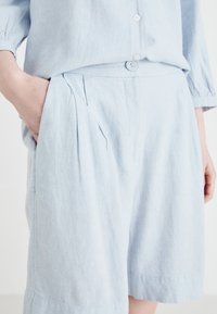 Set di camicia e pantaloni corti in lino azzurro chiaro, caratterizzato da una vestibilità rilassata, dettagli con bottoni, parte anteriore plissettata e tasche laterali, con una finitura morbida e testurizzata.