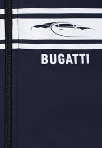 Giacca zip-up navy con strisce bianche e testo "BUGATTI". Presenta una silhouette di pipistrello e tessuto liscio e elasticizzato.