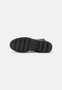 Semelle de chaussure noire avec de profondes rainures horizontales et indication de taille 37, posée sur un fond blanc uni.
