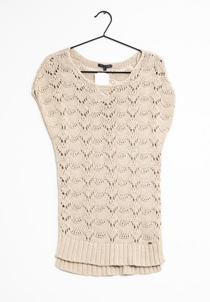 Jersey de punto beige de manga corta con patrón de encaje ondulado y dobladillo acanalado, colgado en una percha negra sobre fondo blanco.