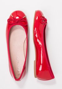 Ett par blanka röda balettflator med små dekorerande rosetter och beige innersulor, visade från ovan och sidan på vit bakgrund.