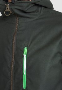 Dark green jacket featuring a zippered front, bright green zipper accent, and a high collar. Made of fabric with a smooth texture.