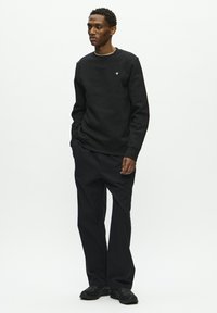 Black sweatshirt with crew neck and small logo, paired with black pants with a straight fit. Features simple design and textured fabric.