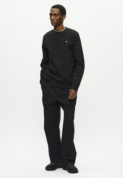 Schwarzer Sweatshirt mit Rundhalsausschnitt und kleinem Logo, kombiniert mit schwarzen, gerade geschnittenen Hosen. Merkmale ein einfaches Design und strukturierten Stoff.