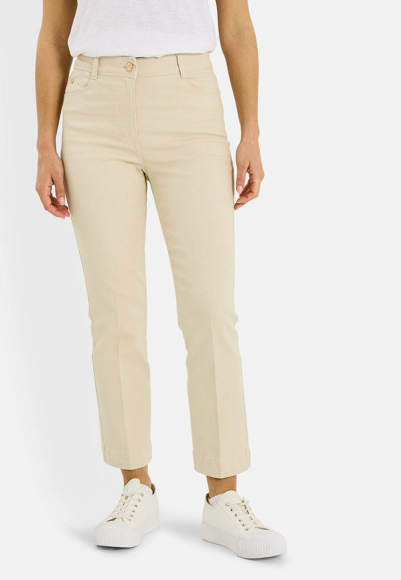Pantalones de algodón beige con un ajuste entallado, cintura de altura media y longitud corta. Combinados con zapatillas blancas con detalles en rosa.