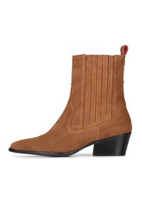 Botines de ante marrón con punta afilada, costuras verticales y un tacón grueso. Presenta una lengüeta roja en la parte posterior.