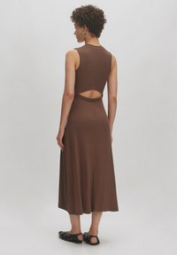 Braunes, geripptes Midikleid mit ärmellosem Design, offenem Rücken und fließender Silhouette. Kombiniert mit schwarzen flachen Schuhen.